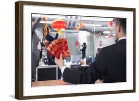 Businessman Holding Red Envelopes and Coworkers Hanging Decorations for Chinese New Year-XiXinXing-Framed Photographic Print