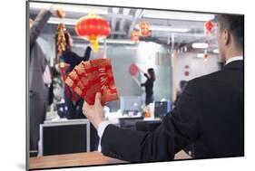 Businessman Holding Red Envelopes and Coworkers Hanging Decorations for Chinese New Year-XiXinXing-Mounted Photographic Print