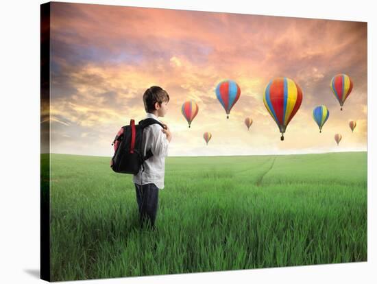 Child Carrying A Backpack Standing On A Green Meadow With Hot-Air Balloons In The Background-olly2-Stretched Canvas