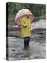 Child in Rain Gear with Umbrella Playing in Puddle.-Nora Hernandez-Stretched Canvas