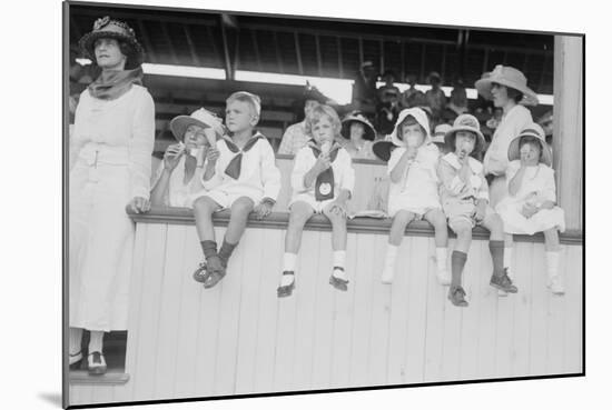 Children Sit on Wall in Front of Stands at the Ballpark and Eat Ice Cream Cones.-null-Mounted Art Print