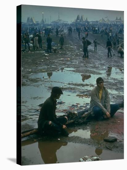 Chuck Morgan Sitting in the Mud and Water with a Friend, During Woodstock Music and Art Fair-John Dominis-Stretched Canvas