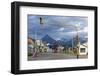 Colourful houses on touristic road framed by traffic lights post with snowy mountain chain beyond, -Fernando Carniel Machado-Framed Photographic Print