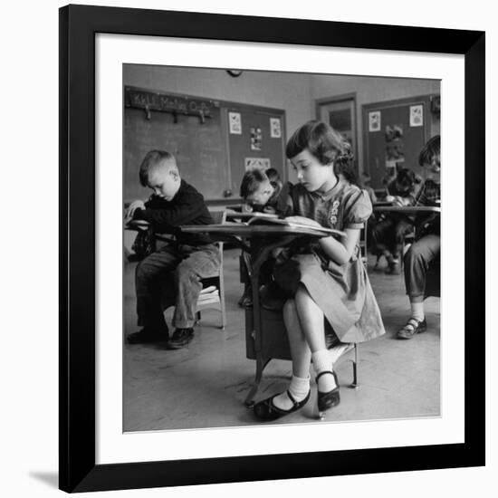 Cute Little Girl Busily at Work, Sitting in a Desk Chair in a Schoolroom, Other Pupils at Work Too-Gordon Parks-Framed Photographic Print