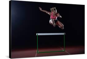 Determined Young Woman Athlete Jumping over a Hurdles-dotshock-Stretched Canvas