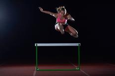 Determined Young Woman Athlete Jumping over a Hurdles-dotshock-Photographic Print