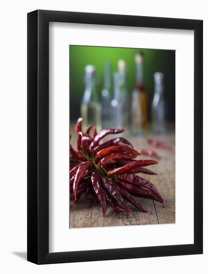 Dried Chillies on Wooden Table, Bottle Against Green Background-Jana Ihle-Framed Photographic Print