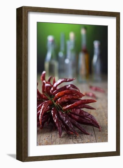 Dried Chillies on Wooden Table, Bottle Against Green Background-Jana Ihle-Framed Photographic Print