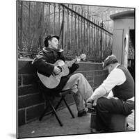 Folk Singer Woody Guthrie Palying His Guitar While Getting a Shoeshine-null-Mounted Premium Photographic Print