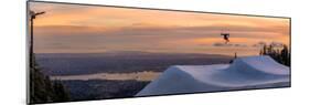 Freestyle skier doing a trick off a jump above city at sunset, Canada, North America-Tyler Lillico-Mounted Photographic Print