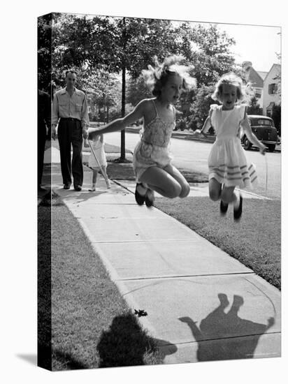 Girls on the street in neighborhood using rope to jump in tandem while man with toddler watches-Alfred Eisenstaedt-Stretched Canvas