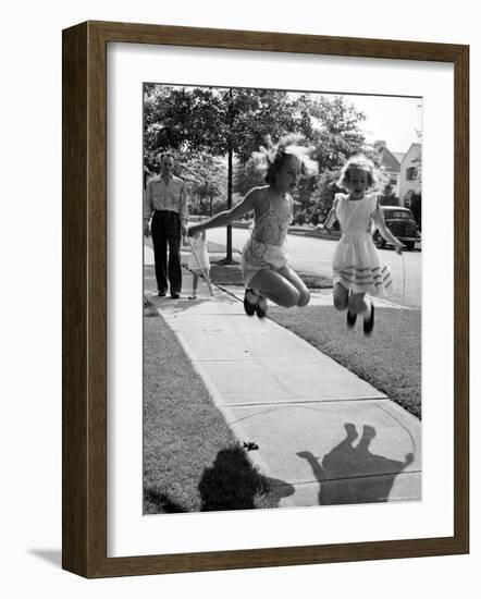 Girls on the street in neighborhood using rope to jump in tandem while man with toddler watches-Alfred Eisenstaedt-Framed Photographic Print