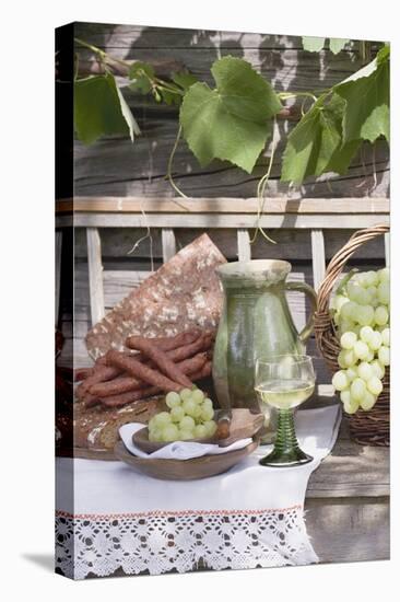 Grapes, Bread, Sausages and Wine on Wooden Bench in Front of Farmhouse-Eising Studio - Food Photo and Video-Stretched Canvas