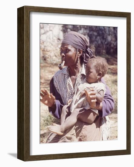 Haitian Woman Smoking a Pipe while Holding a Baby-Lynn Pelham-Framed Photographic Print