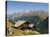 Hiker and Dog on Trail in Front of Traditional Slate Roofed House, Valais, Switzerland-Christian Kober-Stretched Canvas