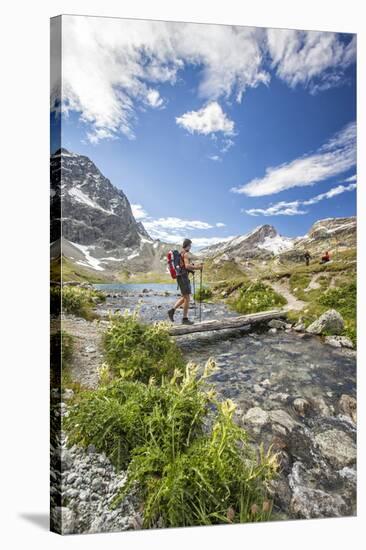 Hiker crossing a stream Engadine Canton of Grisons Switzerland Europe-ClickAlps-Stretched Canvas