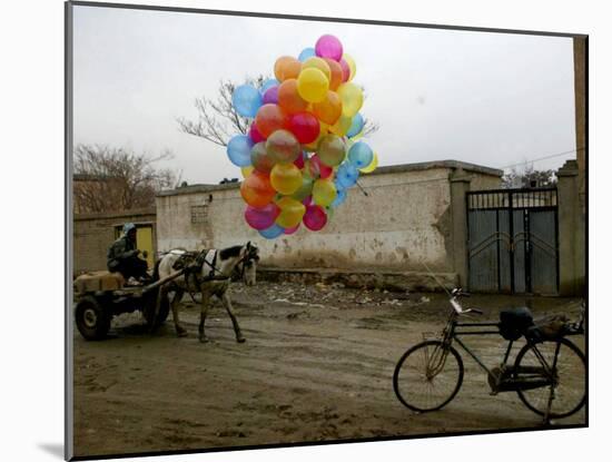 Horse Drawn Cart Drives Past as Balloons Tied to a Bicycle Flutter in the Wind-null-Mounted Photographic Print