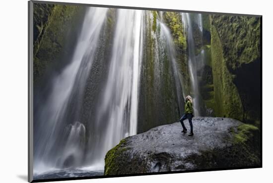 Iceland, Seljalandsfoss. Woman on large rock in front of streaming falls in green slot canyon. (MR)-Mark Williford-Mounted Photographic Print