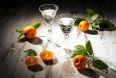 Two Antique Liqueur Glasses with Orange Liqueur and Small Oranges on White Wooden Table-Jana Ihle-Photographic Print