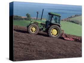 John Deere Tractor with a Rotivator on a Sloping Field in Spring, at Holcombe, Devon, England, UK-Ian Griffiths-Stretched Canvas