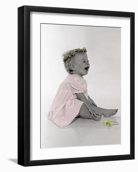 Little Girl Sitting and Laughing with a Floral Ring on Head and Two Flowers in Front of Her-Nora Hernandez-Framed Giclee Print