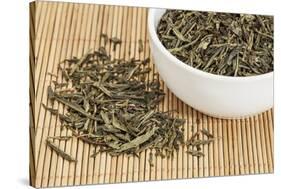 Loose Leaf Sencha Green Tea in a White China Cup and Spilled over Bamboo Mat-PixelsAway-Stretched Canvas