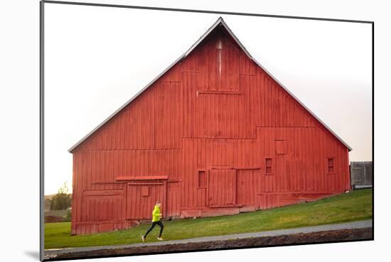 Male Runner Runs Along A Gravel Trail In Front Of Bright Red Barn In UI Arboretum In Moscow, Idaho-Ben Herndon-Mounted Photographic Print