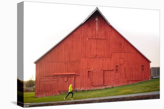 Male Runner Runs Along A Gravel Trail In Front Of Bright Red Barn In UI Arboretum In Moscow, Idaho-Ben Herndon-Stretched Canvas