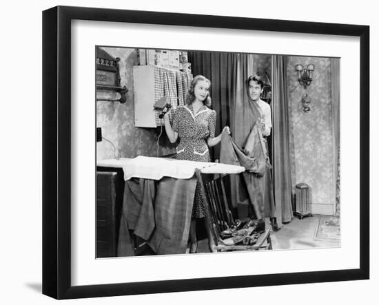Man and Woman Standing in a Kitchen While She is Ironing His Pants and He is Behind a Curtain-null-Framed Photo