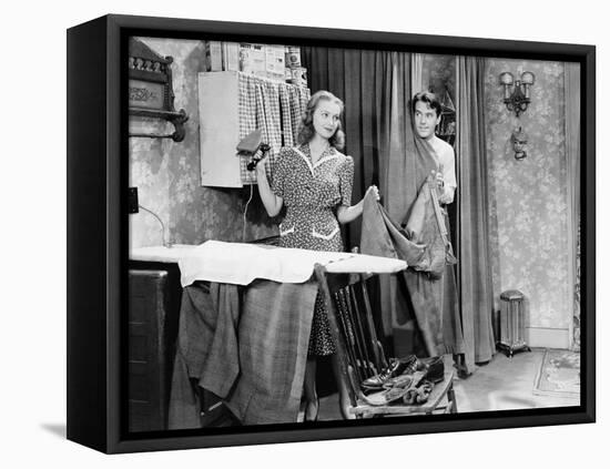 Man and Woman Standing in a Kitchen While She is Ironing His Pants and He is Behind a Curtain-null-Framed Stretched Canvas