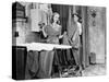 Man and Woman Standing in a Kitchen While She is Ironing His Pants and He is Behind a Curtain-null-Stretched Canvas