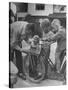 Man Fixing Basket on Bicycle as Children Watch Attentively-Nina Leen-Stretched Canvas