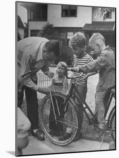 Man Fixing Basket on Bicycle as Children Watch Attentively-Nina Leen-Mounted Photographic Print