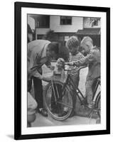 Man Fixing Basket on Bicycle as Children Watch Attentively-Nina Leen-Framed Photographic Print