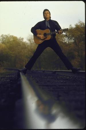 Country/Western Singer Johnny Cash with Guitar Straddling Railroad Tracks