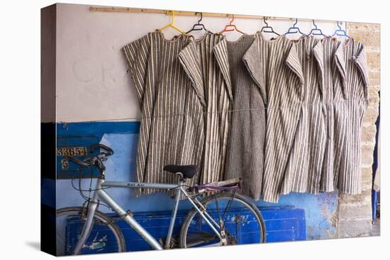 Morocco, Essaouira, Djellabas Hanging on Wall Next to Bicycle-Emily Wilson-Stretched Canvas