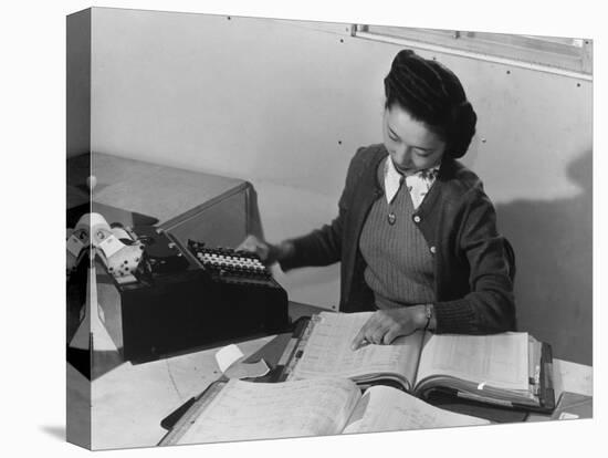 Mrs Teruko Kiyomura, bookkeeper, seated at desk, operating an adding machine while reading a ledger-Ansel Adams-Stretched Canvas