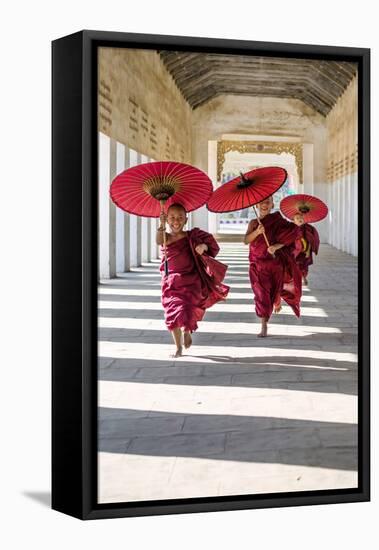 Myanmar, Mandalay Division, Bagan. Three Novice Monks Running with Red Umbrellas in a Walkway (Mr)-Matteo Colombo-Framed Stretched Canvas