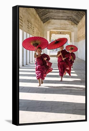 Myanmar, Mandalay Division, Bagan. Three Novice Monks Running with Red Umbrellas in a Walkway (Mr)-Matteo Colombo-Framed Stretched Canvas