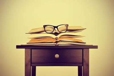 A Pile of Books and a Pair of Eyeglasses on a Desk, Symbolizing the Concept of Reading Habit or Stu