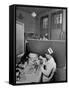 Nurse Sitting at Table with Medical Supplies While Doctors Examine Patient in Background-Wallace Kirkland-Framed Stretched Canvas