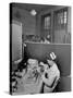 Nurse Sitting at Table with Medical Supplies While Doctors Examine Patient in Background-Wallace Kirkland-Stretched Canvas