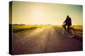 Old Man Riding A Bike On Asphalt Road Towards The Sunny Sunset Sky-Michal Bednarek-Stretched Canvas