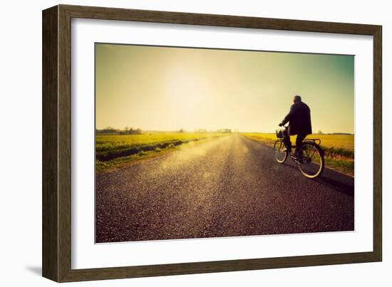 Old Man Riding A Bike On Asphalt Road Towards The Sunny Sunset Sky-Michal Bednarek-Framed Art Print