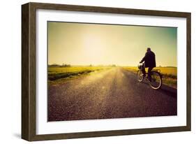 Old Man Riding A Bike On Asphalt Road Towards The Sunny Sunset Sky-Michal Bednarek-Framed Art Print