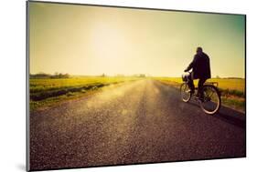 Old Man Riding A Bike On Asphalt Road Towards The Sunny Sunset Sky-Michal Bednarek-Mounted Art Print