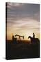 Old West, New West, Man Sitting on Horse with Oil Refinery at Sunset-David R^ Frazier-Stretched Canvas