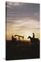 Old West, New West, Man Sitting on Horse with Oil Refinery at Sunset-David R^ Frazier-Stretched Canvas