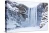 One Person in Red Jacket Walking in the Snow Towards Skogafoss Waterfall in Winter-Neale Clark-Stretched Canvas