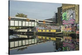 Overground train drives past canal by artists studios and warehouses in Hackney Wick, London, Engla-Julio Etchart-Stretched Canvas